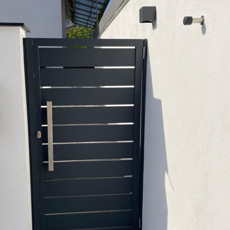 Schwarze Aluminiumtür mit horizontaler Füllung und moderner Griffstange sowie Türstopper an einer weißen Wand.